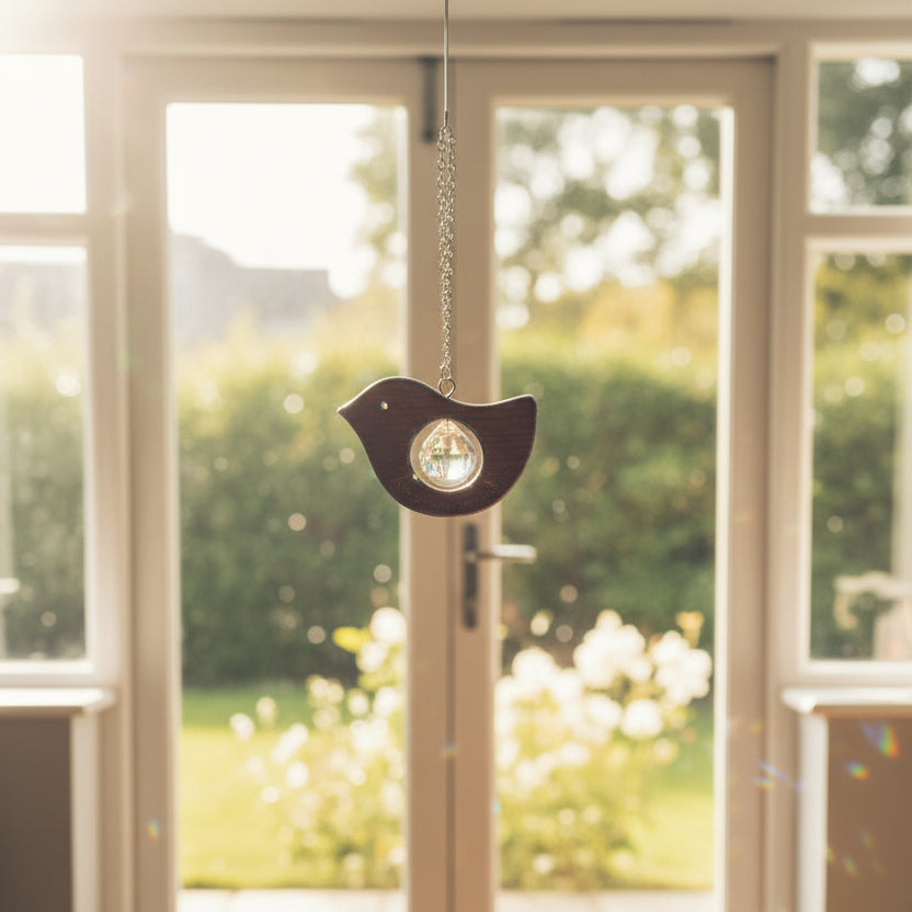 A wooden bird-shaped pendant with a clear faceted crystal center, engraved with 'In Loving Memory of My Mom', hanging from a silver chain against a textured beige fabric background.