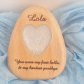 A personalized wooden keepsake plaque shaped like a teardrop, engraved with the name 'Lola' at the top and the quote 'You were my first hello, & my hardest goodbye' at the bottom. The center features a heart-shaped cutout containing a white textured substance.