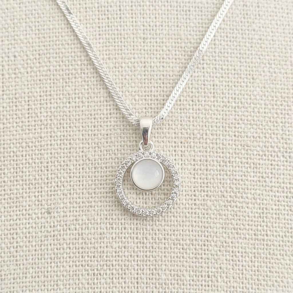 Estelle silver memorial necklace with a pale centre and clear stone surround, displayed on textured beige fabric.